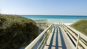 Une promenade en bois qui mène à une plage aux eaux d’un bleu limpide.