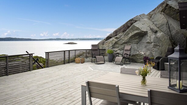 Una terrazza in legno con posti a sedere all'aperto, con vista su uno specchio d'acqua e un paesaggio roccioso.