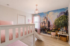 A child's bedroom with a castle mural, a crib, a small table with toys, and a window with curtains.