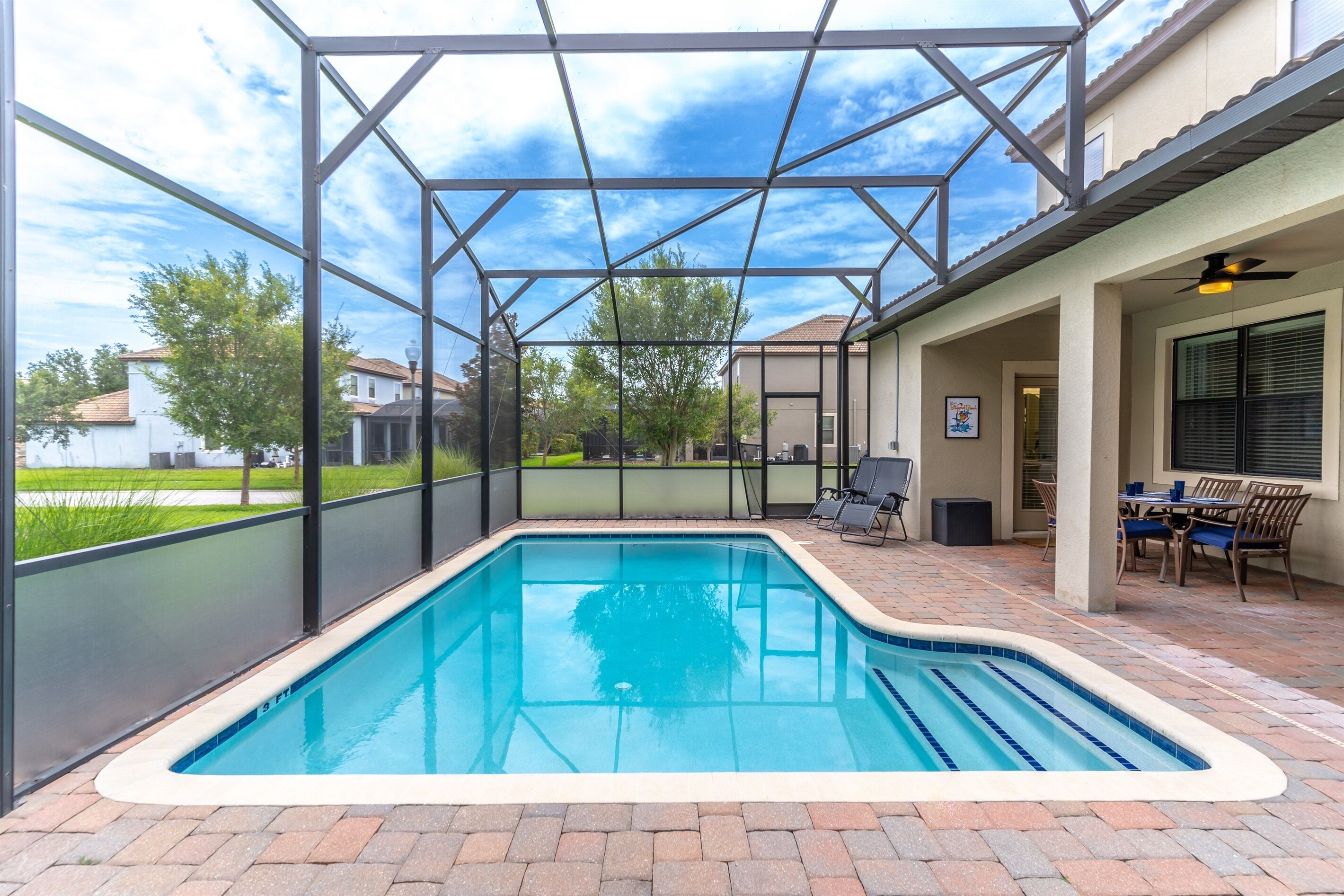 A swimming pool with a glass enclosure, surrounded by a patio area with outdoor furniture and a covered seating area.