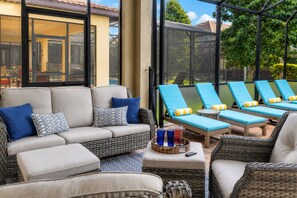 Een zonnig terras buiten met een bank, lounge fauteuils en een tafel met drankjes.