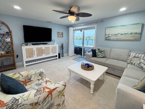 A living room with a TV, sofa, coffee table, and a view of the outdoors.