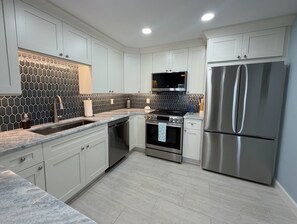 A modern kitchen with white cabinets, a stainless steel refrigerator, a built-in oven, and a microwave.