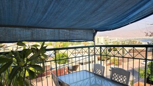 A balcony with a glass table and chairs, a potted plant, and a view of a cityscape. - Melony Apartents Eilot Street Al Hyam (Eilat)