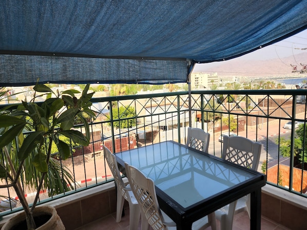 A balcony with a glass table and chairs, a potted plant, and a view of a cityscape.