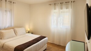 A bedroom with a bed, a bedside table with a lamp, a TV on the wall, and a window with curtains. - Melony Apartents Eilot Street Al Hyam (Eilat)