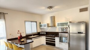 A modern kitchen with a central island, stainless steel appliances, and yellow bar stools. - Melony Apartents Eilot Street Al Hyam (Eilat)