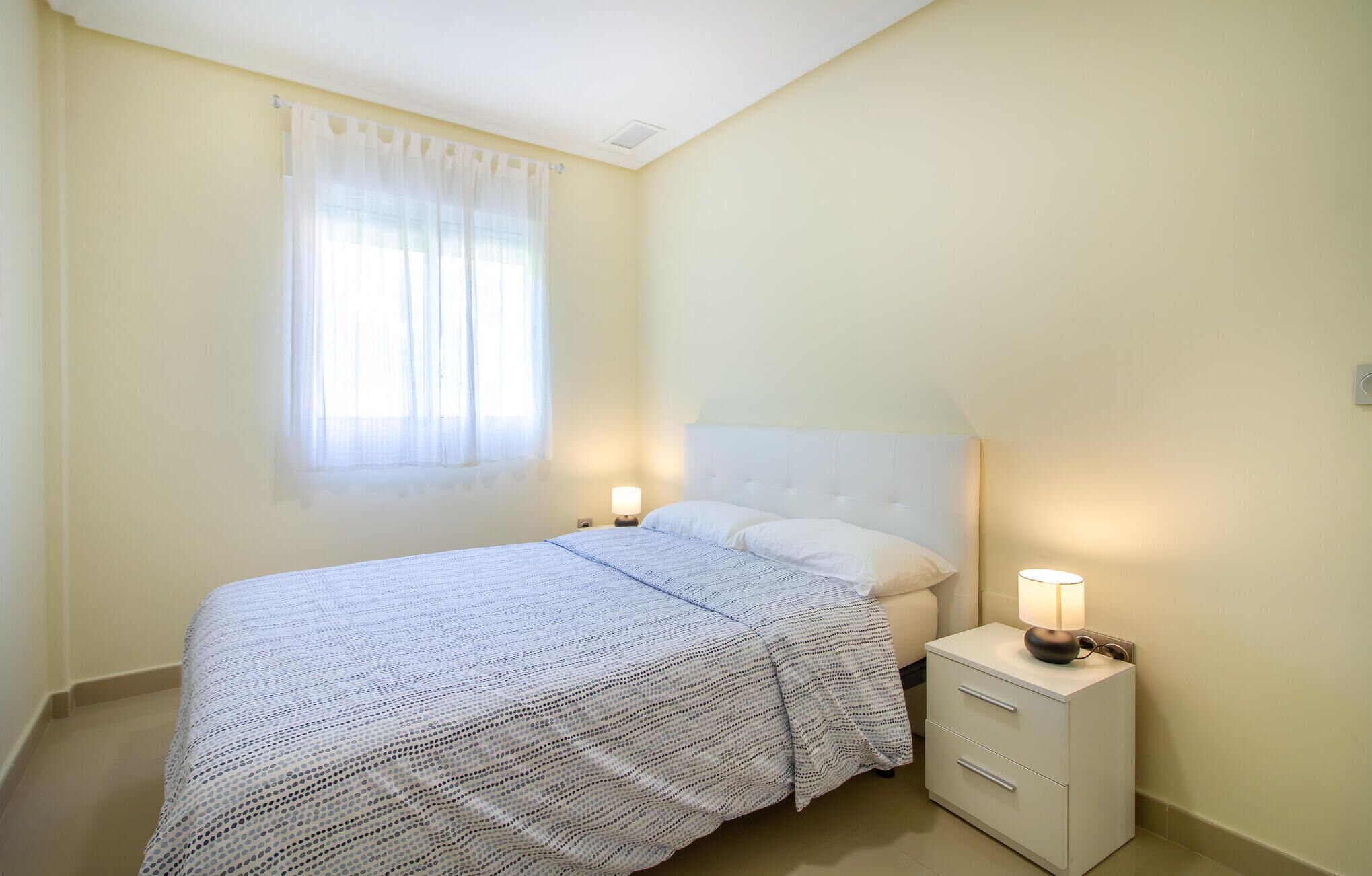 Een slaapkamer met een bed, nachtkastje en een raam met gordijnen.
