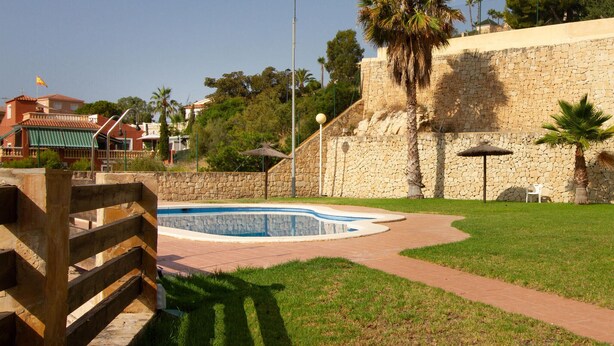 A swimming pool surrounded by stone walls, a grassy area, and a few palm trees. - 5 bedroom gorgeous home in El Campello (El Campello)
