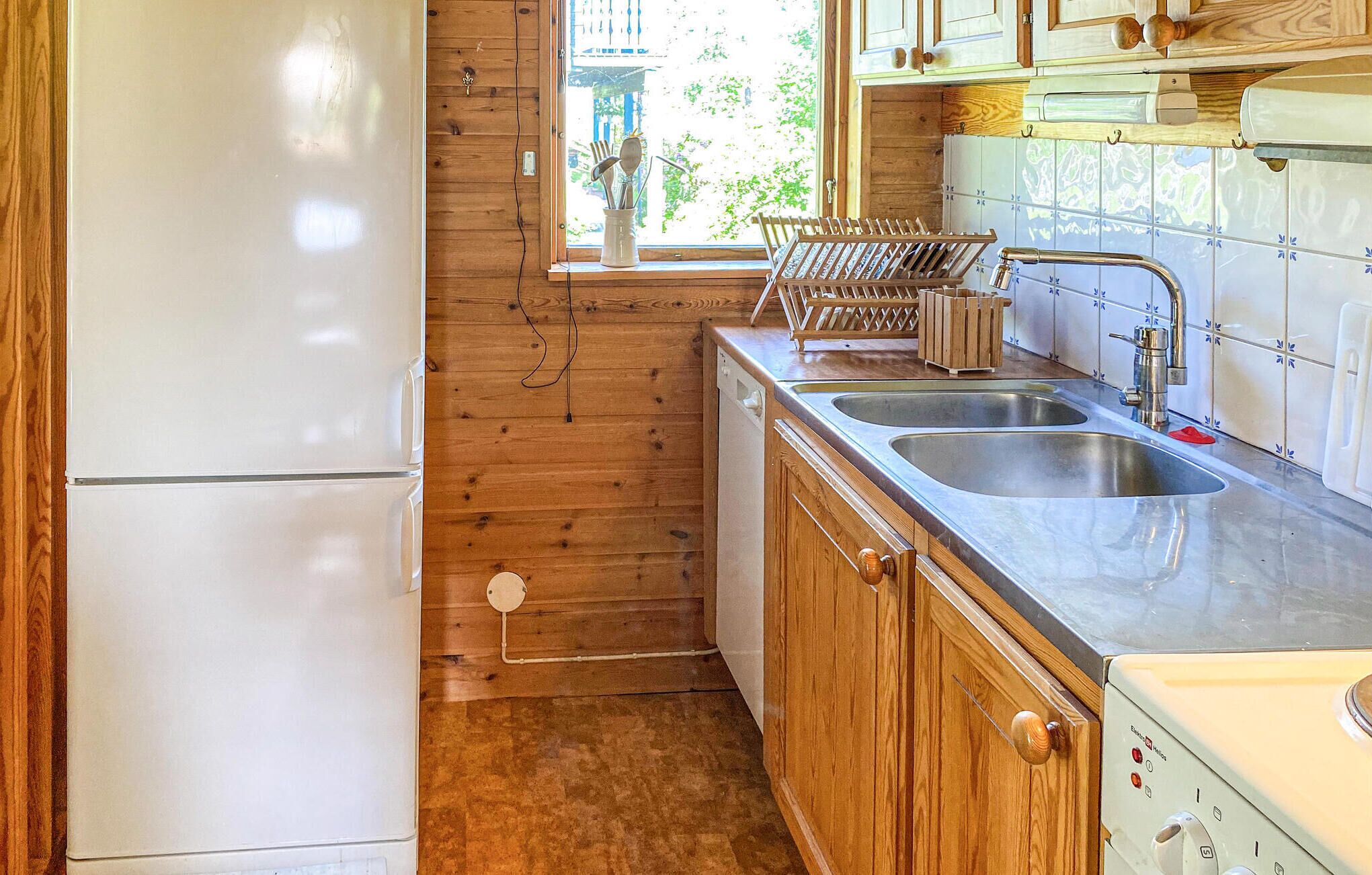 Eine kleine Küche mit Holzausstattung, einem doppelten Becken und einem weißen Kühlschrank.