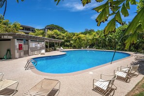 A swimming pool with lounge chairs and a covered area, surrounded by greenery.