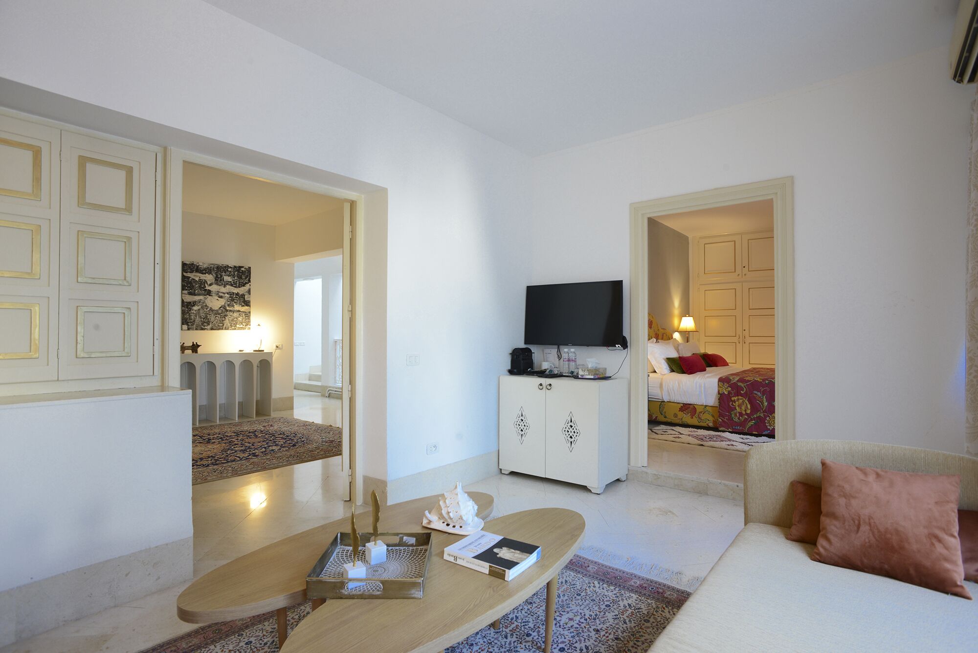 Una sala moderna con sofá, mesa de centro y televisor. Hay un mueble con televisor de pantalla plana y una cama con colcha estampada.