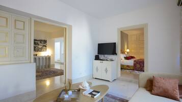 Una sala moderna con sofá, mesa de centro y televisor. Hay un mueble con televisor de pantalla plana y una cama con colcha estampada.
