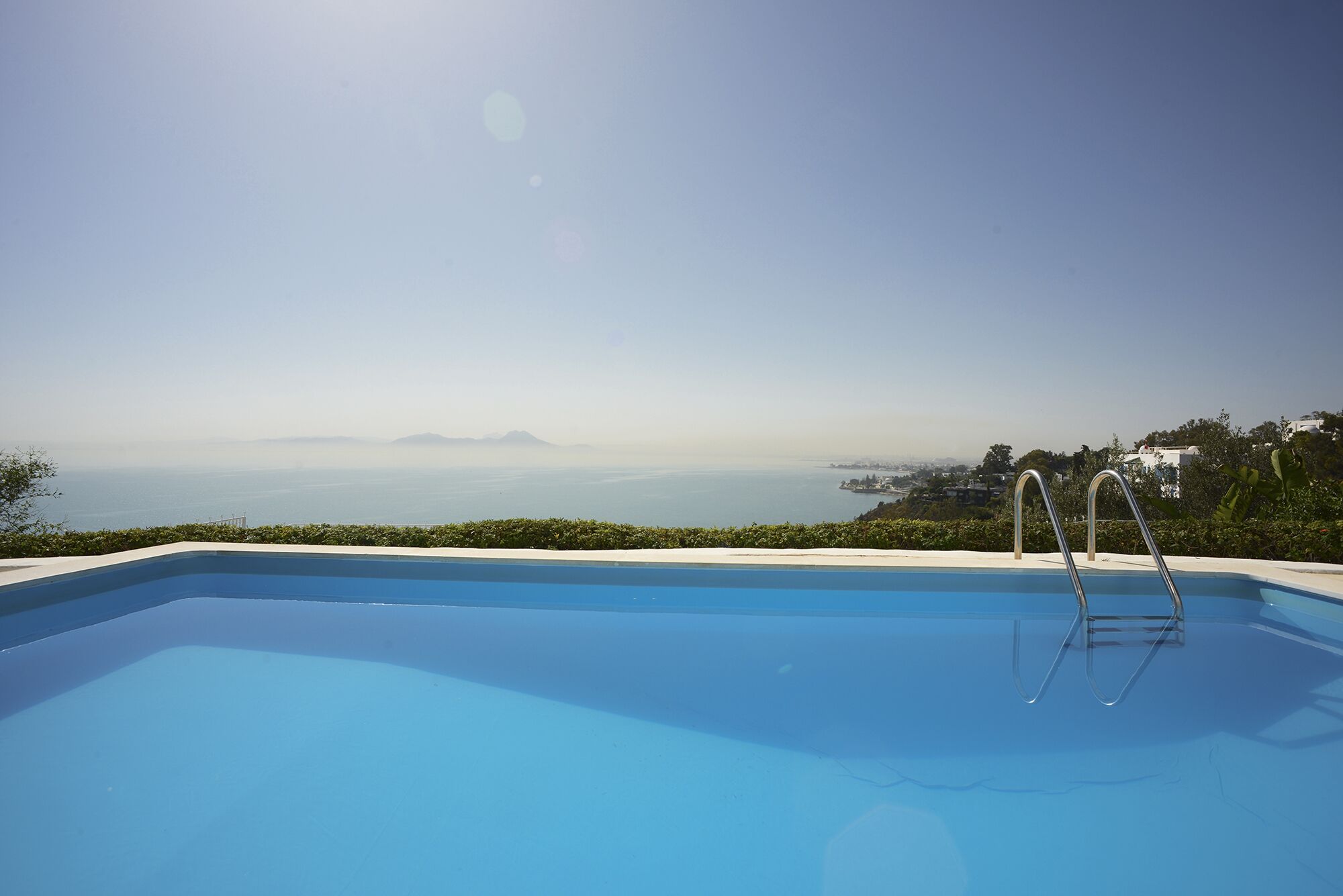 Une piscine d’un bleu éclatant, offrant une vue sur la mer et les montagnes lointaines.