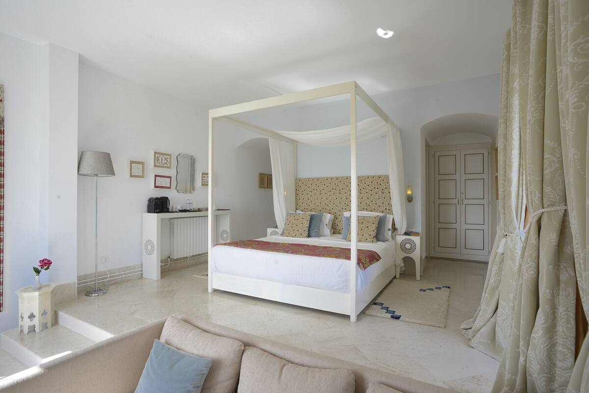 Quarto com cama de dossel, mesa de cabeceira, abajur e guarda-roupa.
