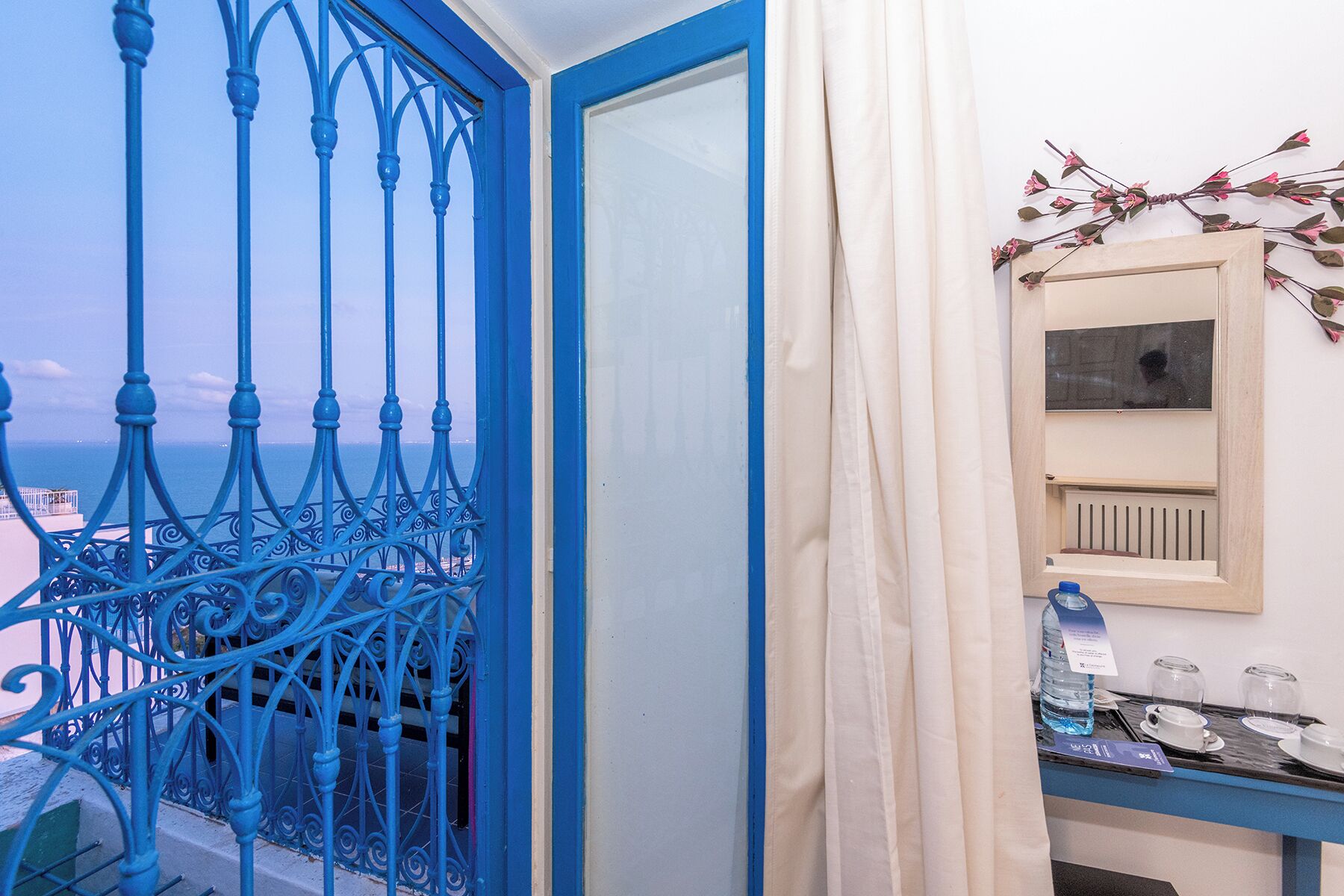 A balcony with blue wrought iron railings, a white door, and a view of the sea.