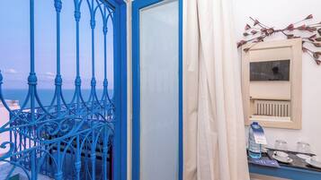 A balcony with blue wrought iron railings, a white door, and a view of the sea.