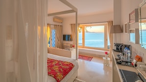 A hotel room with a bed, a desk with a computer, a TV, and a view of the sea.