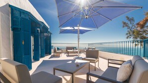 A terrace with outdoor seating, a large umbrella, and a view of the sea.