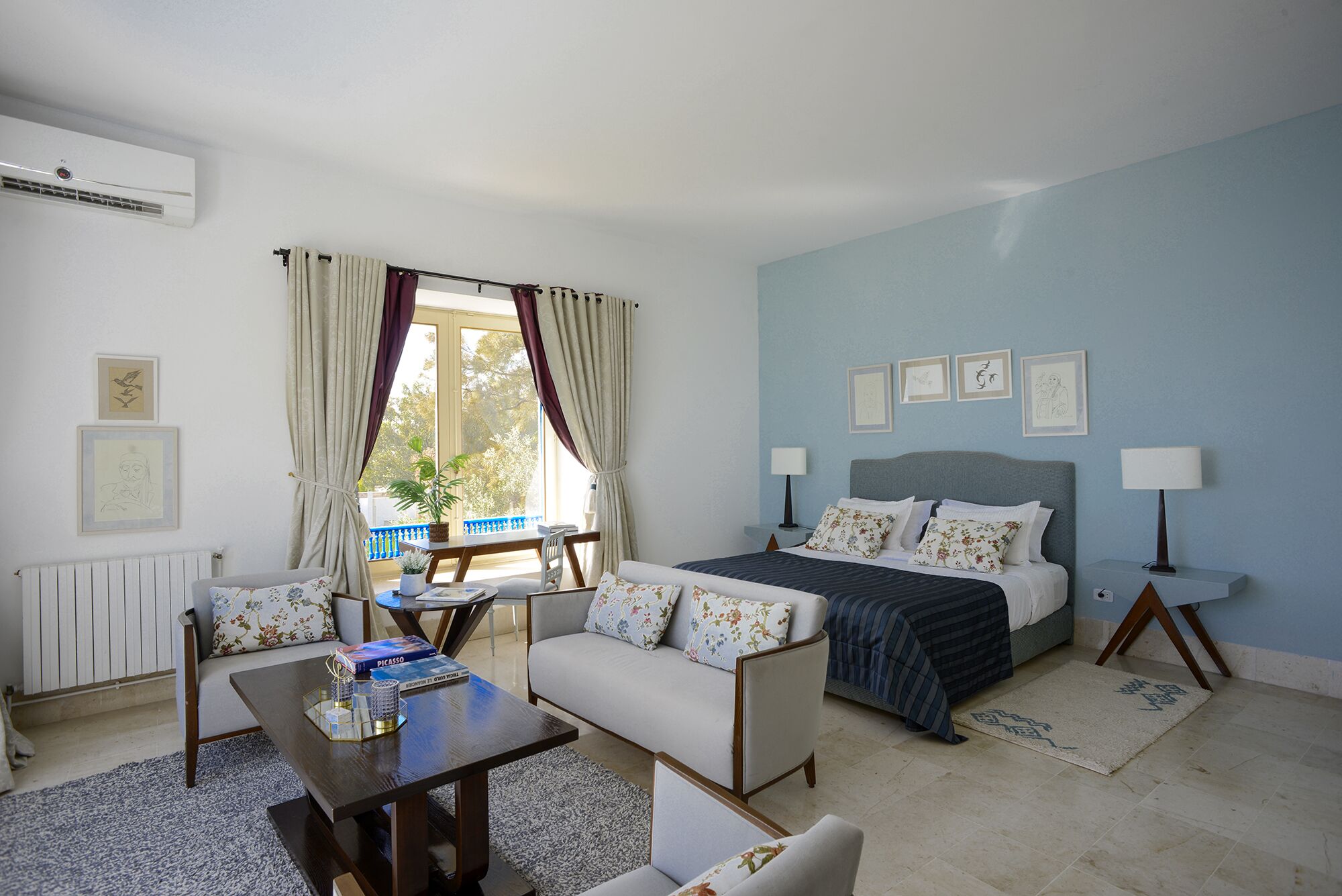 A bedroom with a bed, two bedside tables, a sofa, a coffee table, and a window with curtains.