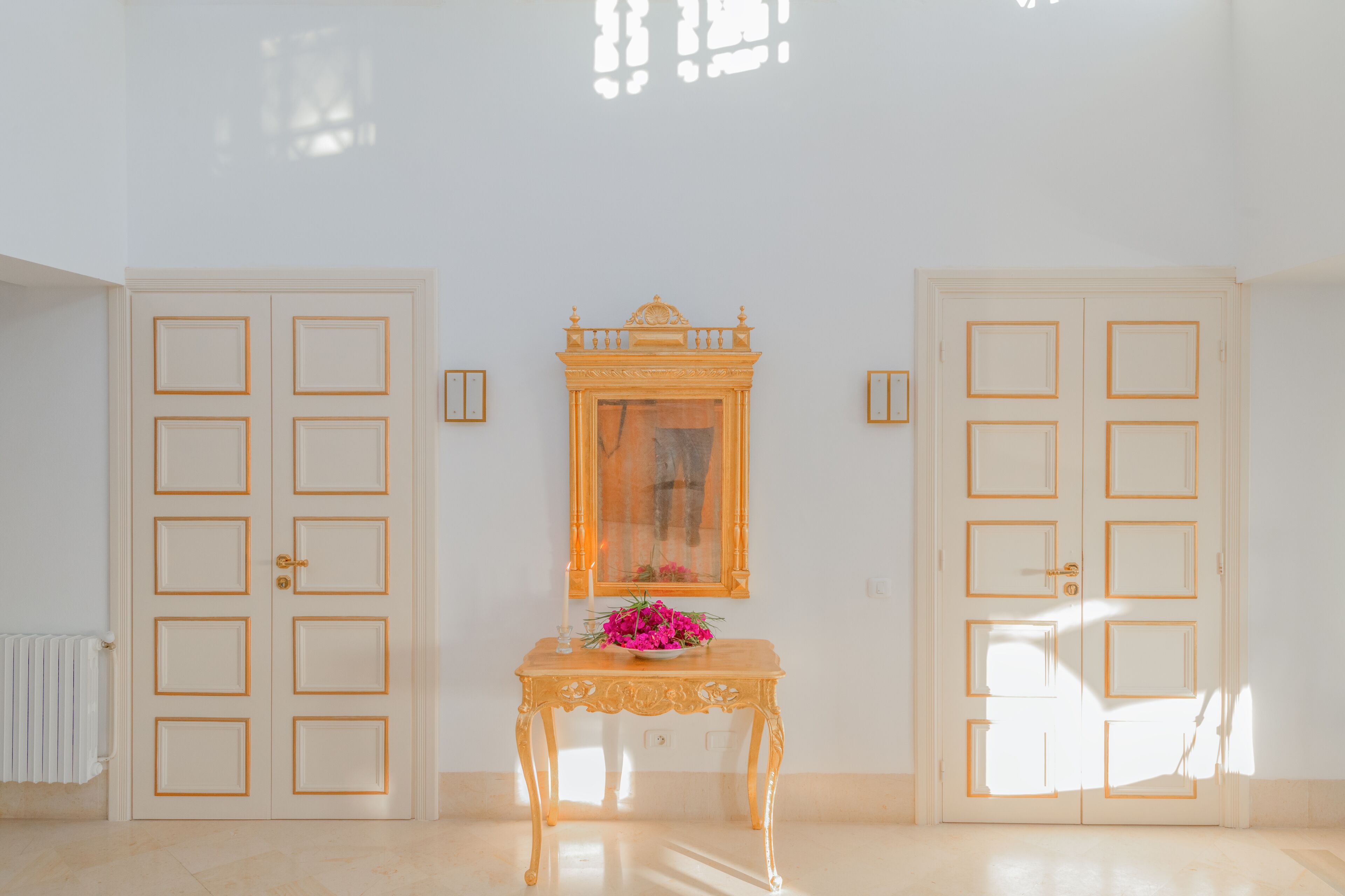 A room with two doors, a table with a vase of flowers, and a mirror on the wall.