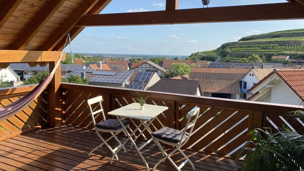 Una terraza de madera con una mesa y sillas, con vista a una zona residencial con paneles solares en los tejados.