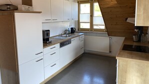 Una cocina compacta con armarios blancos, una cafetera y una ventana con persianas.