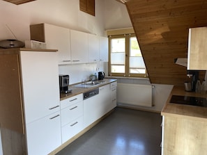Una cocina compacta con armarios blancos, una cafetera y una ventana con persianas.