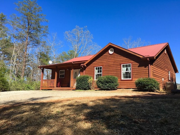 A wooden cabin with a red roof, a porch, and a small garden area.