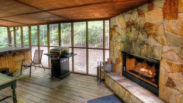 A covered outdoor area with a stone fireplace, a grill, and a dining table with chairs.