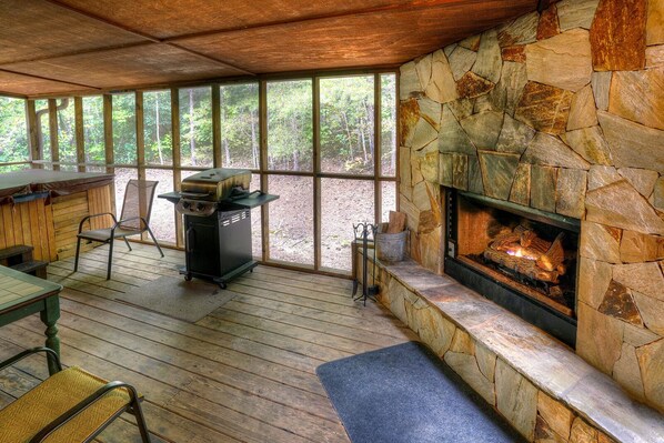 A covered outdoor area with a stone fireplace, a grill, and a dining table with chairs.