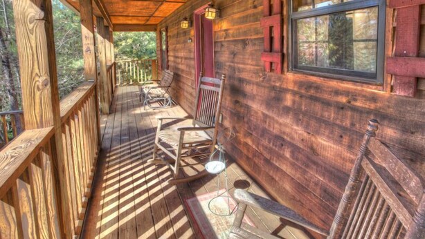 A wooden porch with rocking chairs and a small table, surrounded by a wooden railing.