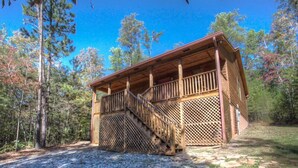 A wooden cabin with a staircase leading to a porch, surrounded by trees.