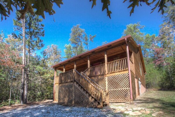 Une cabane en bois avec un escalier menant à une véranda, le tout entouré d’arbres.