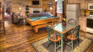 A cozy cabin interior with a pool table, seating area, and kitchen.