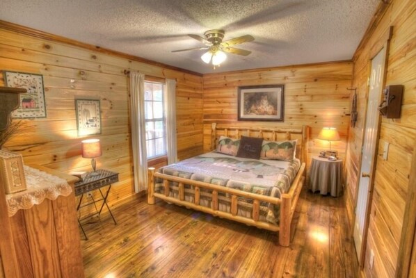 A wooden cabin bedroom with a bed, two bedside lamps, a ceiling fan, and a framed picture on the wall.