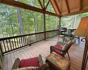 A covered deck with wooden flooring, wicker furniture, and a table with a painting.