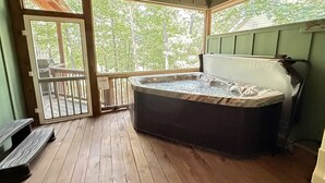A hot tub in a wooden room with a view of trees.