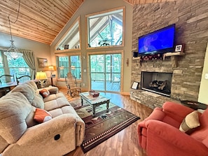 A spacious living room with a fireplace, large windows, and a television.