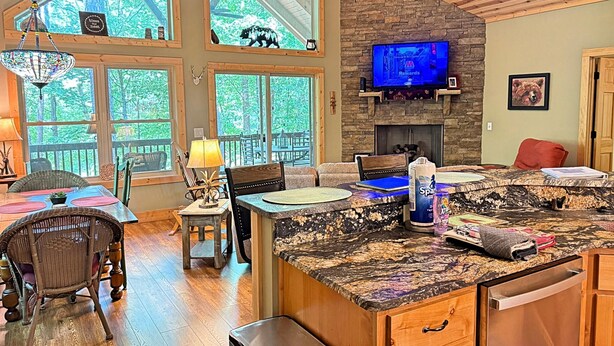 A spacious living area with a stone fireplace, a television mounted above it, and a large window overlooking a forested area.