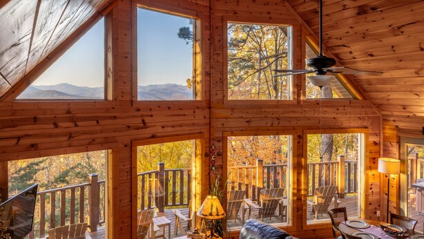 Une cabane dotée de nombreuses grandes fenêtres offrant une vue sur les montagnes, d’un ventilateur de plafond et d’une terrasse avec des sièges d’extérieur.
