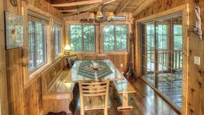 A wooden cabin interior with a large dining table, benches, and large windows offering views of the forest. - Delaine`s Retreat - 4 BR Cabin, Dog Friendly, Walkable to Downtown Helen, GA (Helen)