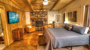 A cozy bedroom with a stone fireplace, a bed with a quilted cover, a television on the wall, and wooden furniture. - Delaine`s Retreat - 4 BR Cabin, Dog Friendly, Walkable to Downtown Helen, GA (Helen)