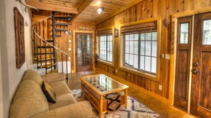 A cozy cabin interior with a wooden staircase, a glass-top coffee table, and a sofa. - Delaine`s Retreat - 4 BR Cabin, Dog Friendly, Walkable to Downtown Helen, GA (Helen)