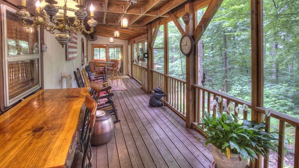 A wooden deck with a dining table and chairs, surrounded by windows offering a forest view. - Delaine`s Retreat - 4 BR Cabin, Dog Friendly, Walkable to Downtown Helen, GA (Helen)