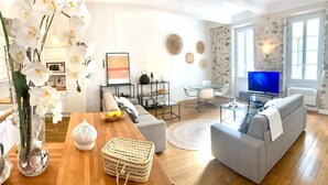 A modern living room with a sofa, coffee table, and decorative items. There is a television and a dining area with a table and chairs. - (008) Cosy & Chic Old Town (Antibes)