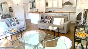 A modern living room with a glass dining table, two sofas, and a kitchen area with white cabinets and a wooden countertop. - (008) Cosy & Chic Old Town (Antibes)