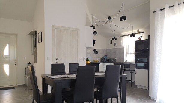 Un comedor moderno con una mesa rectangular y seis sillas, una cocina con horno empotrado y microondas, y una lámpara en el techo.