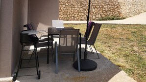 Un patio al aire libre con una mesa, sillas, un paraguas grande y un muro de piedra.