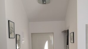 Un pasillo con una puerta blanca, una pequeña mesa con un farol y cuadros en las paredes.